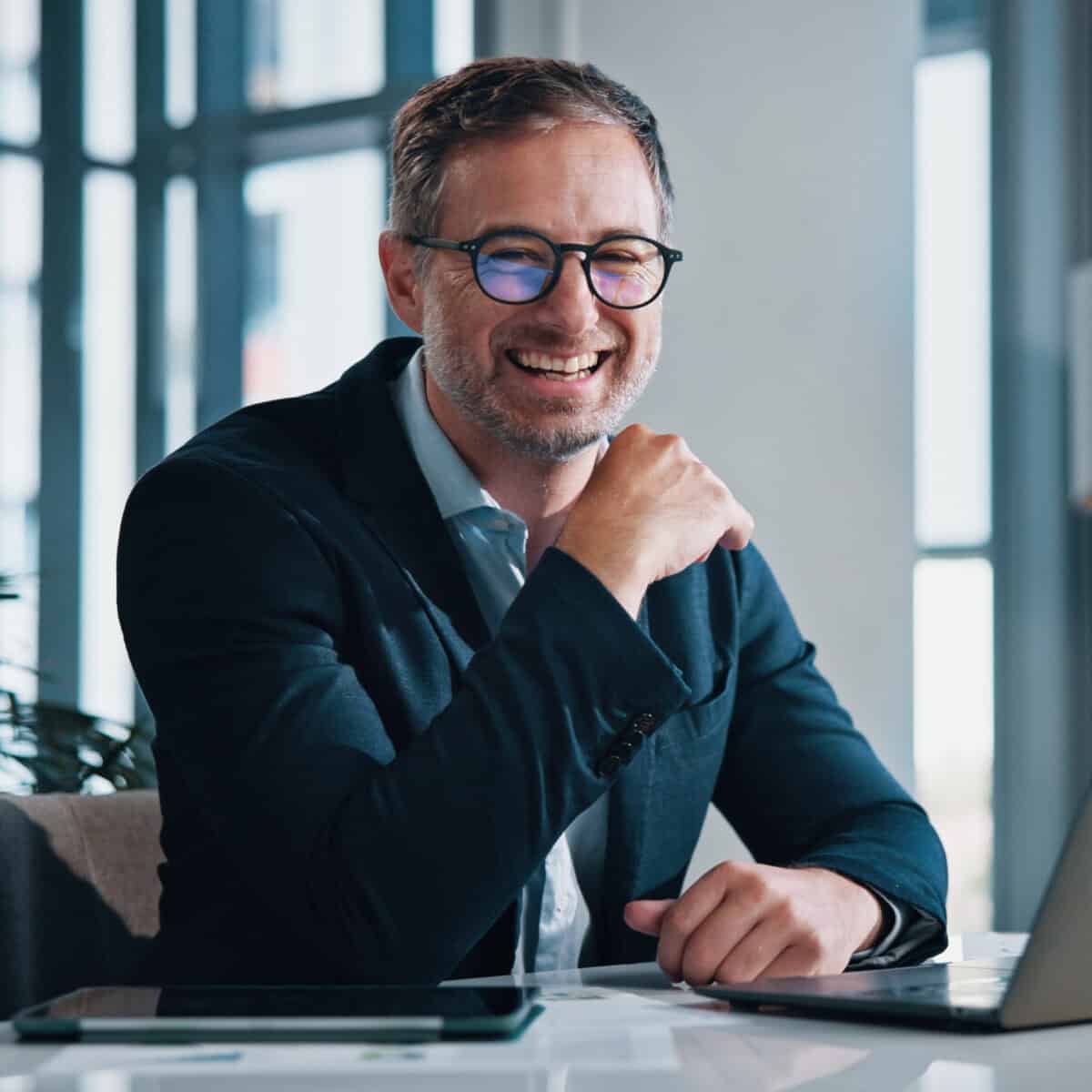 Hymyilevä liikemies työskentelee kannettavalla tietokoneella – 99,9 % käyttöaikatakuu Avosorsan webhotellipalvelussa.